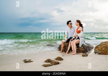 Giovane coppia che si aggirano sulla roccia della spiaggia di mare a Koh MunNork Island, Rayong, Thailandia Foto Stock