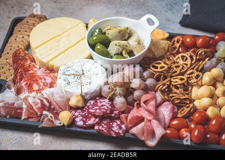 Piatto di salumi e formaggi. Vassoio di antipasti con carni assortite, formaggi, frutta, olive e cracker. Foto Stock