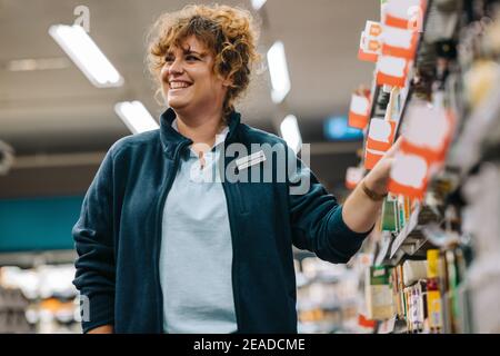 Lavoratore femminile che lavora in negozio. Responsabile del negozio di alimentari in piedi in corridoio e sorridente. Foto Stock