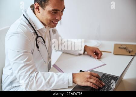 Medico concentrato utilizzando il computer portatile mentre si lavora alla scrivania armadio Foto Stock