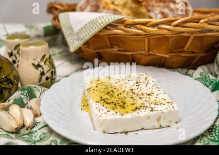 Focalizzazione selettiva del formaggio greco feta condito con olio d'oliva e origano con pane croccante fatto in casa sullo sfondo Foto Stock