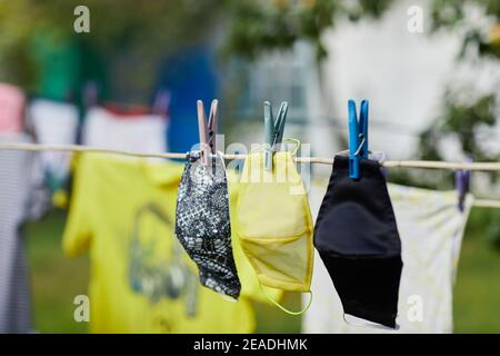 Concetto di coronavirus. Diversi tipi di maschere facciali protettive fatte a mano appese su una corda all'aperto Foto Stock