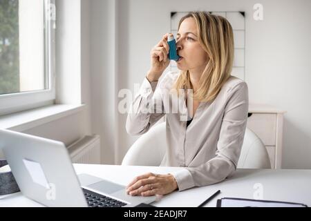 Donna d'affari con inalatore di asma alla sua scrivania in ufficio Foto Stock