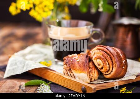 Dolci fatti in casa alla cannella e cardamomo (panini) e una tazza di caffè nero Foto Stock