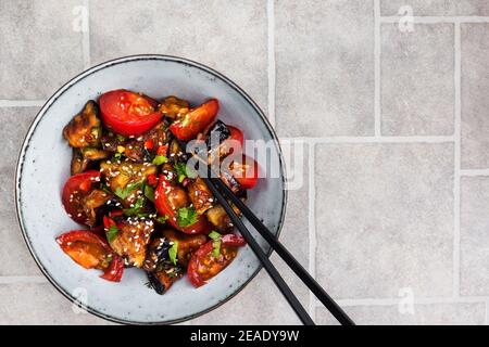 Primo piano di melanzane in stile cinese con sesamo, peperoncino e pomodori, vista dall'alto, spazio copia Foto Stock