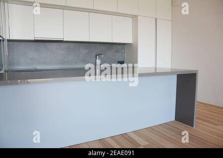 Design moderno minimalista della cucina con armadi bianchi, cappa di gamma, frigorifero incorporato, ripiano grigio con un lavello e piano cottura elettrico e un Foto Stock