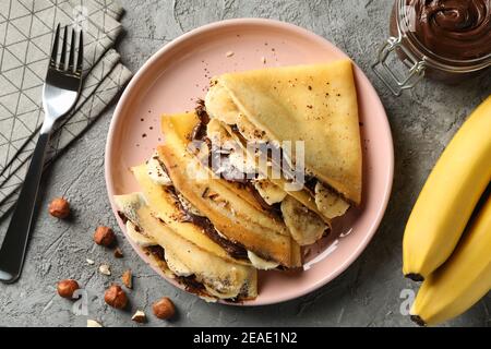 Concetto di deliziosa colazione con crepes con pasta di cioccolato, banana e noci su sfondo grigio Foto Stock