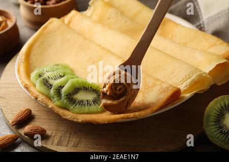 Concetto di colazione con crepes con kiwi e cucchiaio con burro di arachidi Foto Stock