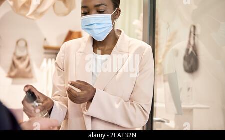 Proprietario di un negozio afroamericano che igienizza le mani di un cliente Foto Stock