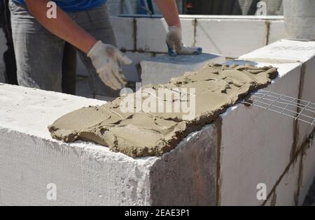 Un appaltatore di costruzione sta applicando mortaio con un mortaio di vanga per murklay un muro di una nuova costruzione della casa da blocchi di calcestruzzo di gas. Foto Stock