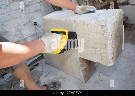 Un appaltatore di edifici sta tagliando blocchi di calcestruzzo cellulare autoclavati, calcestruzzo a gas utilizzando una sega manuale in un cantiere. Foto Stock