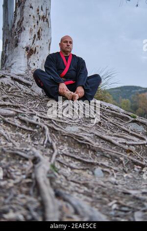 artista marziale meditando in un lago con nero e rosso kimono Foto Stock