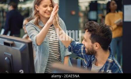 Biblioteca universitaria: Ragazza caucasica brillante e ragazzo di talento Studio per gli esami e dare alto cinque dopo il compito risolto con successo. Lavorare sull'assegnazione, utilizzare Foto Stock