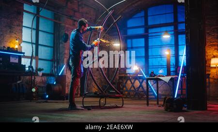 Handsome Male Artist utilizza un smerigliatore angolare per creare brutali sculture in metallo in Studio. Hipster Guy lucida tubo di metallo con Sparks Flying Off esso Foto Stock