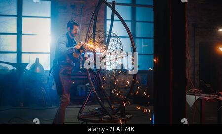 Il talento Emerging Male Artist utilizza un Disc Grinder per creare una brutale scultura in metallo astratta che riflette il momento presente. Bell'uomo Foto Stock