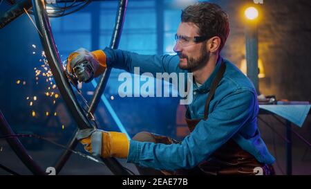 Handsome Male Artist utilizza un smerigliatore angolare per creare una moderna brutale scultura in metallo in Studio. Hipster Guy. Fabricator contemporaneo che crea astratto Foto Stock