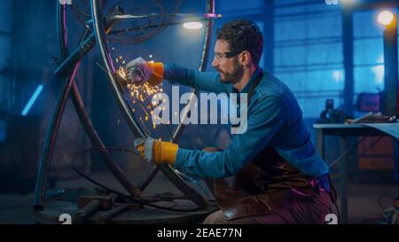 Handsome Male Artist utilizza un smerigliatore angolare per creare una moderna brutale scultura in metallo in Studio. Hipster Guy. Fabricator contemporaneo che crea astratto Foto Stock