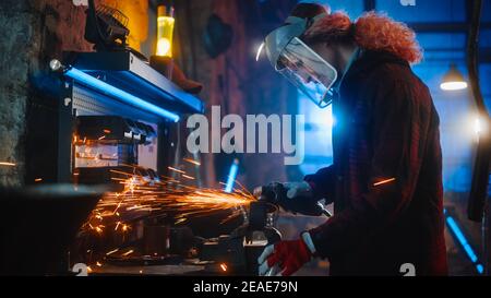 La talentuosa Female Fabricator utilizza una smerigliatrice angolare per lucidare un oggetto metallico circolare. L'anello è afferrato in una morsa da banco. Bellissimo Tomboy Engineer Foto Stock