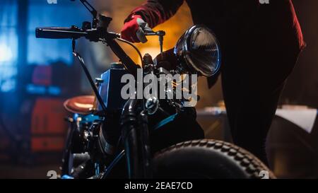 Primo piano riprese di un appassionato di motociclette meccaniche in guanti da lavoro rossi in un garage o in un laboratorio creativo. Persona di talento che lavora su una bici personalizzata con un Foto Stock