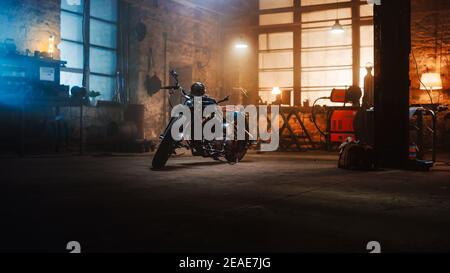 Moto Bobber personalizzata in piedi in un autentico laboratorio creativo. Motocicletta in stile vintage sotto la lampada calda in un garage. Foto Stock