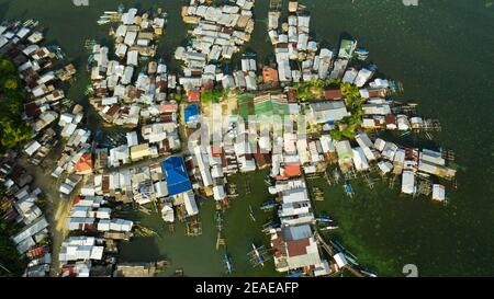 Una piccola barca Outrigger ormeggiata vicino a una casa su palafitte in un villaggio di pescatori. Villaggio costiero di pescatori. Filippine, Mindanao. Foto Stock