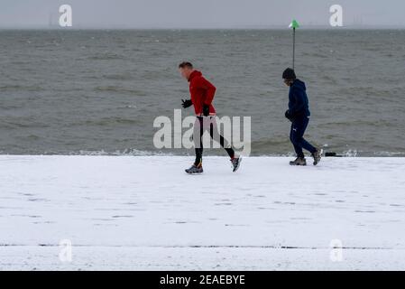 Southend on Sea, Essex, Regno Unito. 9 Feb 2021. Storm Darcy ha lasciato cadere ulteriore neve sul lungomare, e ha portato condizioni ghiacciate e ventose. Joggers e escursionisti hanno sfidato i venti freddi lungo Western Esplanade sul lungomare Foto Stock