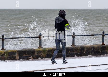 Southend on Sea, Essex, Regno Unito. 9 Feb 2021. Storm Darcy ha lasciato cadere ulteriore neve sul lungomare, e ha portato condizioni ghiacciate e ventose. Joggers e camminatori hanno sfidato i venti freddi e le onde che si infrangono lungo la Western Esplanade Foto Stock