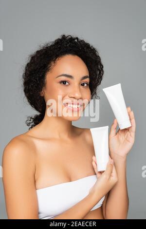 Giovane donna afroamericana che tiene tubi con schiuma detergente isolato su grigio Foto Stock