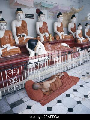 Myanmar, Yangon, Shwedagon Pagoda, monaco buddista dormendo di fronte alle statue di Buddha Foto Stock