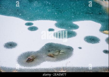 Nevicate pesanti su un lago di montagna trasparente, in parte ghiacciato e blu profondo in Vallese Foto Stock