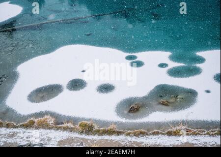 Nevicate pesanti su un lago di montagna trasparente, in parte ghiacciato e blu profondo in Vallese Foto Stock