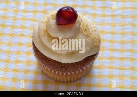Biscake, biscotto incontra cupcake, Cake-well di ciliegia da M&S Set su serviette di tovagliolo giallo e bianco controllato Foto Stock