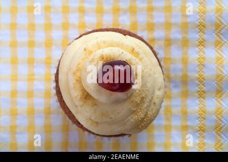 Biscake, biscotto incontra cupcake, Cake-well di ciliegia da M&S Set su serviette di tovagliolo giallo e bianco controllato Foto Stock