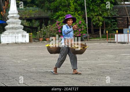 Donna laotiana con cestini di trasporto sopra la sua spalla di ritorno dallo shopping nel mercato verde, Luang Prabang, Laos Foto Stock