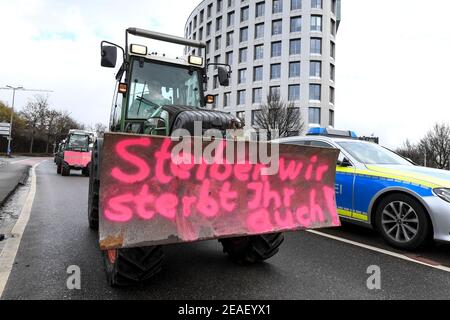 Friedrichshafen, Germania. 09 febbraio 2021. Con l'iscrizione 'se moriamo, anche tu muori' sulla parte anteriore del trattore, un agricoltore dimostra nei dintorni dell'ufficio amministrativo distrettuale nel distretto del lago di Costanza contro la legge prevista per la protezione degli insetti. Circa 150 agricoltori con i loro trattori fanno il giro intorno all'ufficio amministrativo del distretto. Credit: Felix Kästle/dpa/Alamy Live News Foto Stock