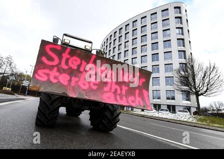 Friedrichshafen, Germania. 09 febbraio 2021. Con l'iscrizione 'se moriamo, anche tu muori' sulla parte anteriore del trattore, un agricoltore dimostra nei dintorni dell'ufficio amministrativo distrettuale nel distretto del lago di Costanza contro la legge prevista per la protezione degli insetti. Circa 150 agricoltori con i loro trattori fanno il giro intorno all'ufficio amministrativo del distretto. Credit: Felix Kästle/dpa/Alamy Live News Foto Stock