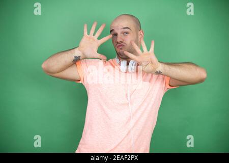 Giovane uomo calvo che usa le cuffie su sfondo verde mostrando e. puntare con le dita numero nove mentre sorridendo sicuro e. felice Foto Stock