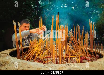 Hong Kong, Cina. Il Monastero buddista di po Lin, Isola di Lantou. Un ospite che brucia i bastoni dell'incenso. Foto Stock