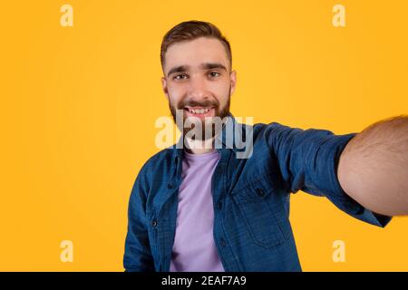 Bel giovane ragazzo caucasico che prende selfie e sorride ampiamente orange studio sfondo Foto Stock
