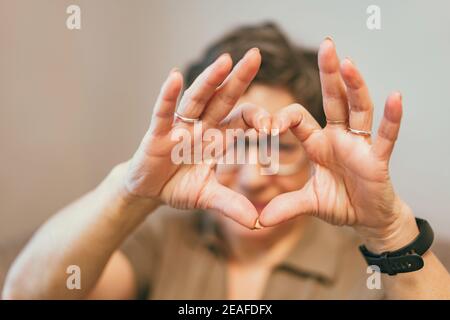 Carino anziana donna che fa una forma del cuore con lei mani e dita Foto Stock