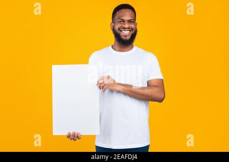 Allegro uomo africano mostrando Poster di carta in piedi su sfondo giallo Foto Stock