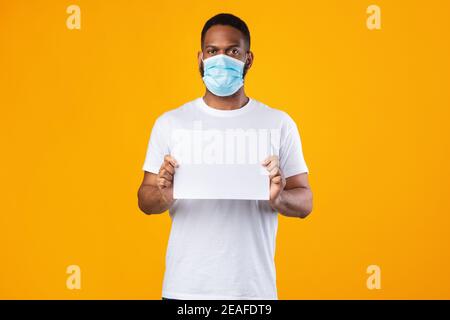 Uomo Africano che indossa maschera facciale che mostra la lavagna bianca, sfondo giallo Foto Stock