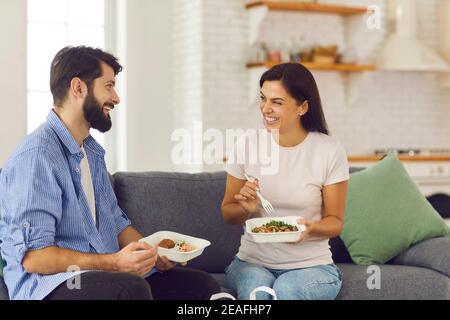 Giovane coppia sorridente uomo e donna seduta a casa e. mangiare cibo sano in scatola Foto Stock