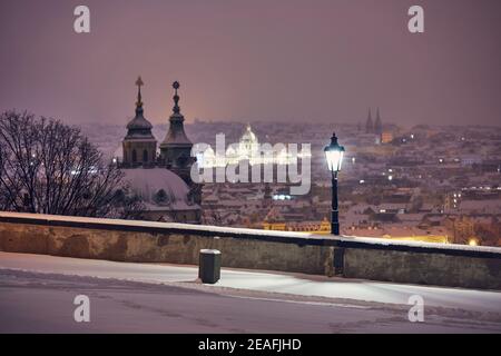 Vista della strada illuminata contro la città innevata di notte. Paesaggio urbano di Praga in inverno, Repubblica Ceca Foto Stock