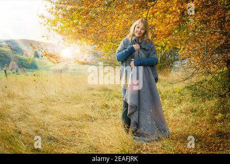 Una donna di 40 anni nel paesaggio naturale autunnale. La donna bionda indossa abiti in lana e stivali. Ha una coperta. Foto Stock