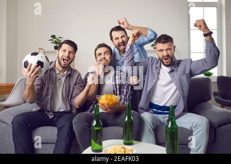 Amici maschili che celebrano l'obiettivo delle squadre preferite durante la visione della televisione di calcio corrispondenza Foto Stock