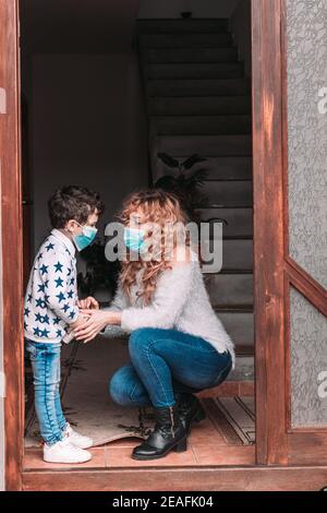 Mamma e suo figlio del bambino indossano maschere facciali che si preparano per uscire Foto Stock