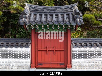 Cancello di legno rosso sotto il tetto di tegole in muro di pietra. Architettura orientale tradizionale. Busan, Corea del Sud Foto Stock