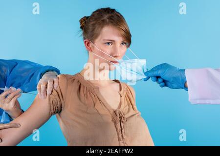 Vittoria sul coronavirus. Pandemic Covid-19. Donna bionda seria dopo il vaccino del coronavirus. La mano del medico toglie la maschera medica sterile protettiva Foto Stock