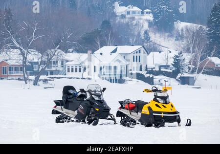 2 febbraio 2019- Grandes-Piles, QC, Canada: Due motoslitte parcheggiate su un lago ghiacciato e le case sullo sfondo, Mauricie Foto Stock